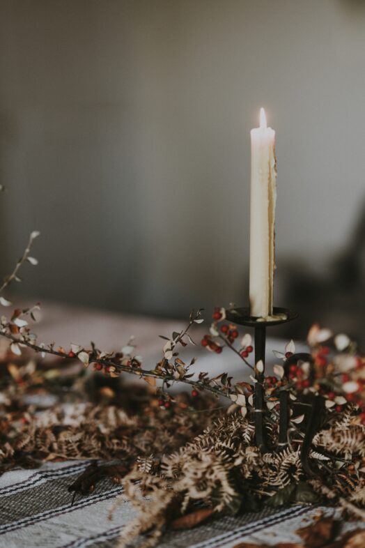 Ett ensamt tänt ljus står i en ljusstake omgiven av torkade blommor.